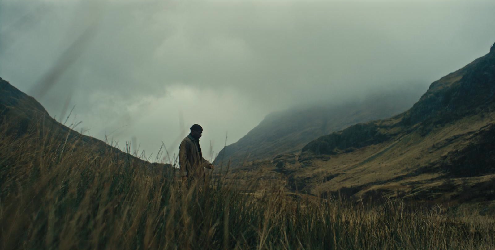 Alexis Ffrench walking through long grass in a misty Scottish Highlands valley